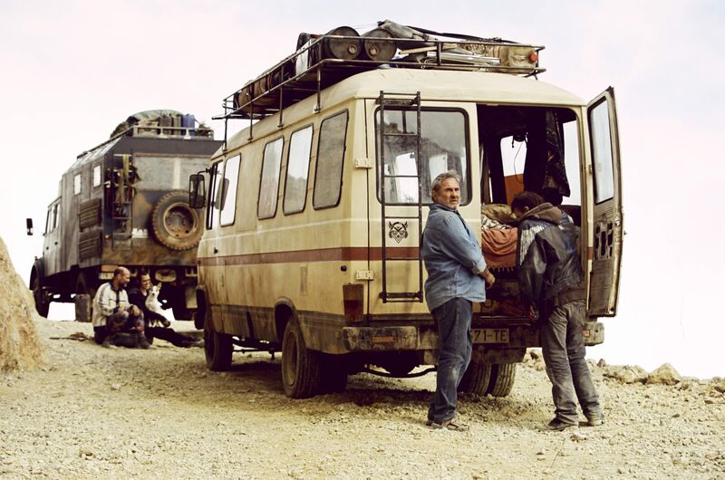 Two men stand outside a dirty campervan in the desrt