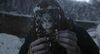 A person with blue hands holds a scary photo of a corpse up to their face