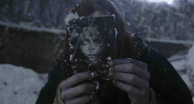 A person with blue hands holds a scary photo of a corpse up to their face