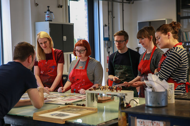 A group of adults around a workshop desk, learning about Lino printing.