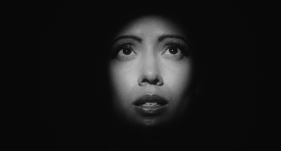 A woman's face peers through the darkness, concerned.