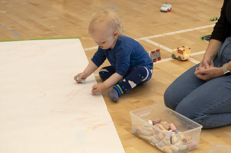 Child drawing with chalk on a piece of paper taped to the floor
