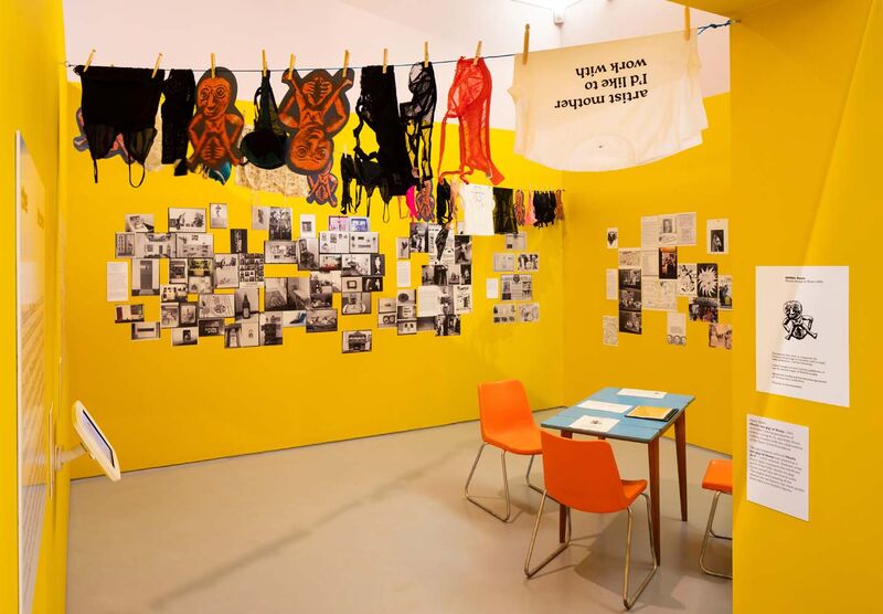 A yellow room with laundry hanging from ceiling and black and white images and text on the walls. A table with handouts is also on it