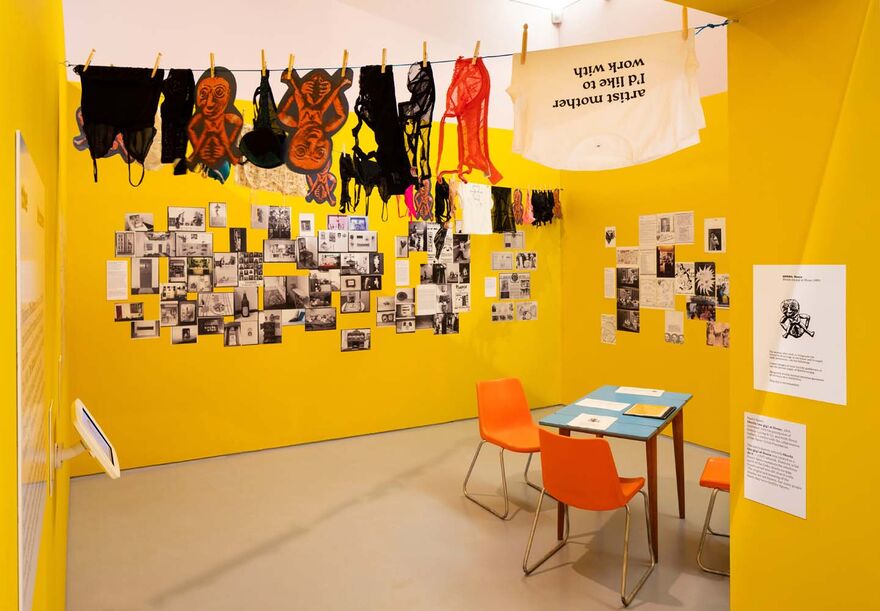 A yellow room with laundry hanging from ceiling and black and white images and text on the walls. A table with handouts is also on it