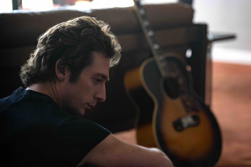 A man sits on the floor next to a guitar