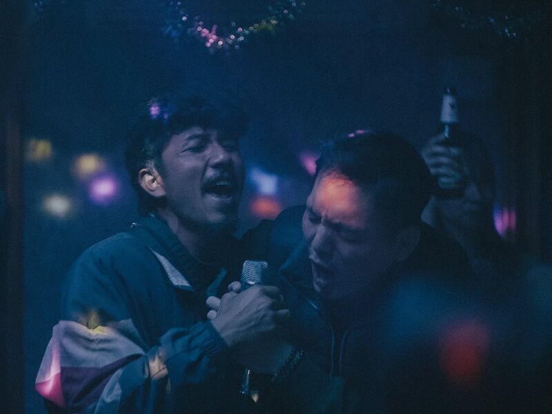 Two men sing karaoke together in a dark room.