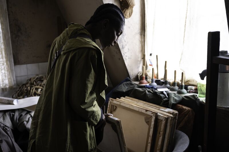 A woman is looking through various canvases stored together in an art studio