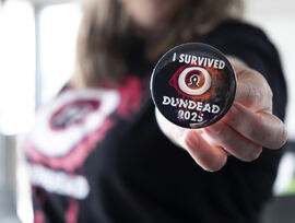 Person holding a I SUVIVED DUNDEAD 2025 badge