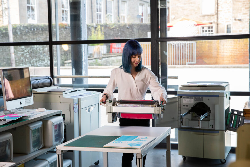 Photo of Katie Ravenscraig loading a riso ink drum into the Riso machine in DCA Print Studio