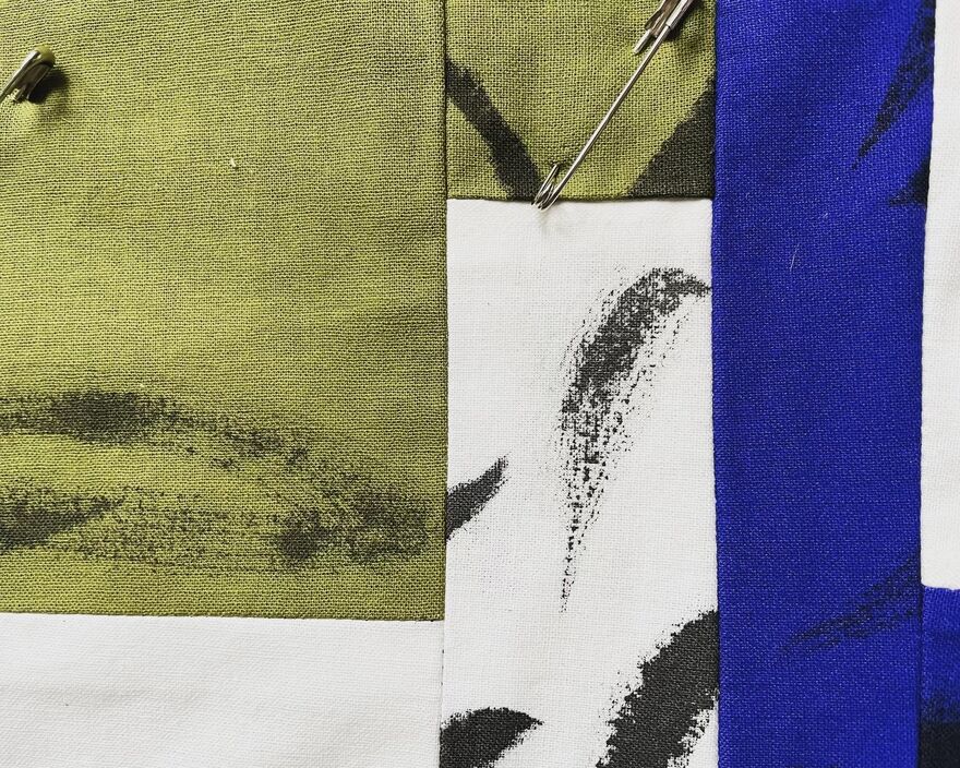 a close up of a patterned quilt, with rectangles in blue, green and whilte with black paint strokes