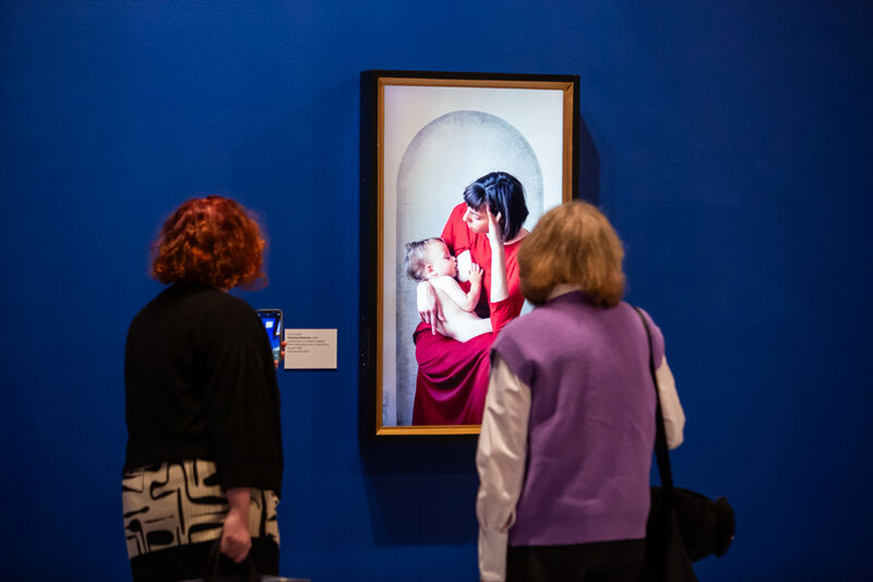 An image of a women breastfeeding a baby on a blue gallery wall