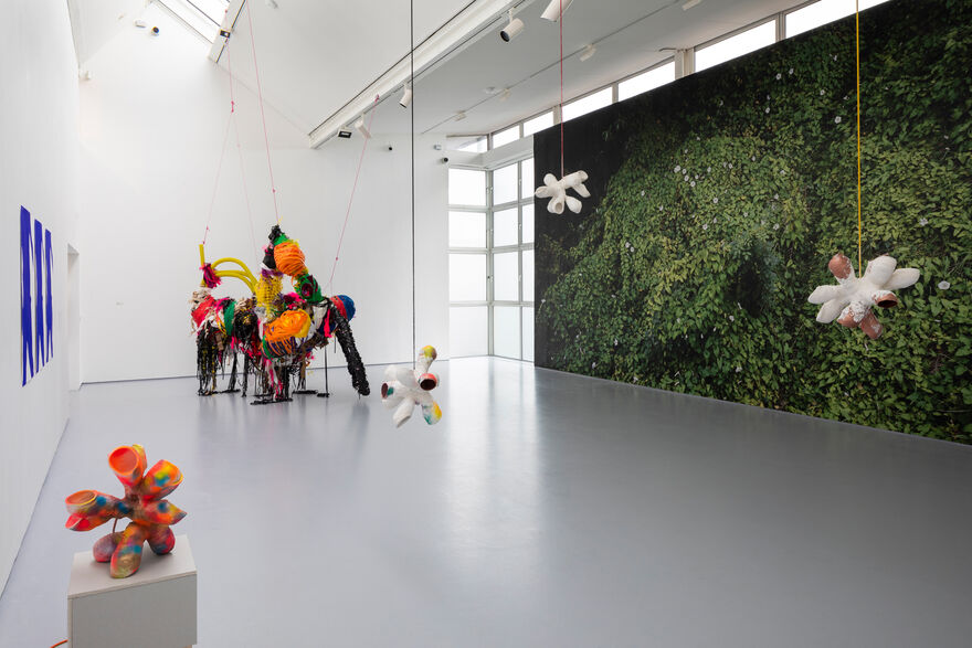A wall with the image of a plant covering it and colourful hanging sculptures suspected from the ceiling