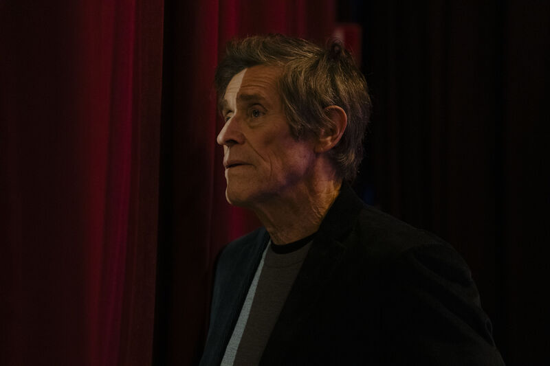 A man looks sadly through a gap in stage curtains