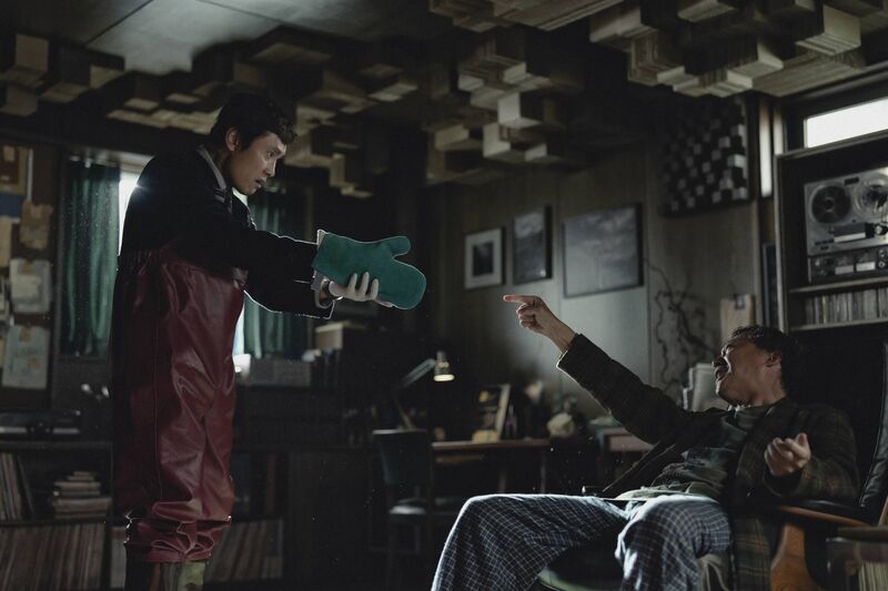 A man points a gun muffled by an oven glove at another man who laughs and points at him