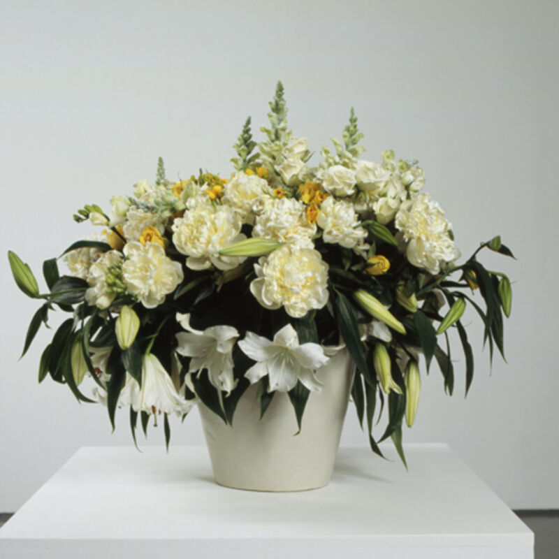 From Marine Hugonnier's exhibition. A white pot is filled with a large assortment of drooping flowers, which includes white and yellow lines and roses.