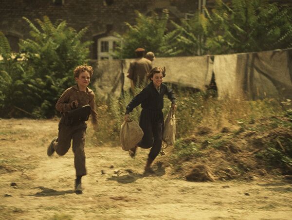 Two children run along a grassy road.