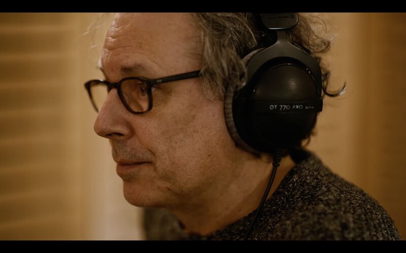 An older man wearing glasses and headphones can be seen from close up