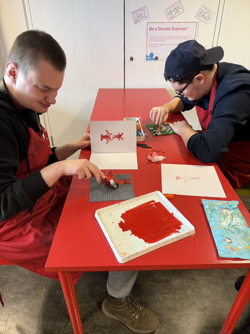 Two people at a table making prints with lego