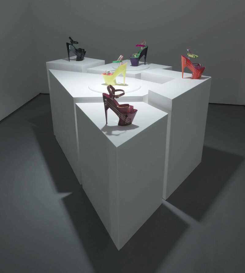 A white table display a collection of the world’s first wireless high-heeled shoe guitar, which are brightly coloured with a very high heel.