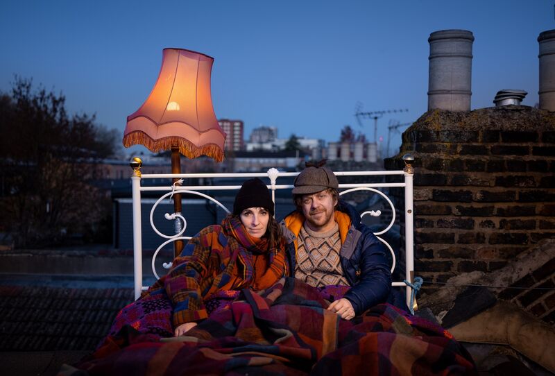A couple in a bed perched on top of a roof at night