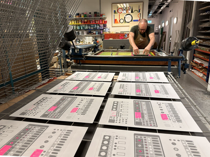 Person screen printing while earlier prints dry on the rack in DCA Print Studio
