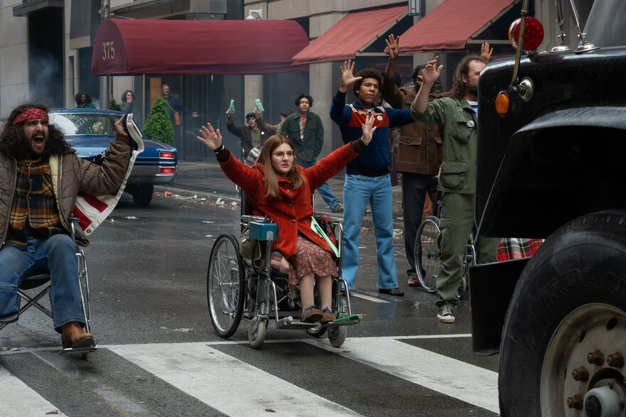 People in wheelchairs sit in protest at a crossing to stop a lorry