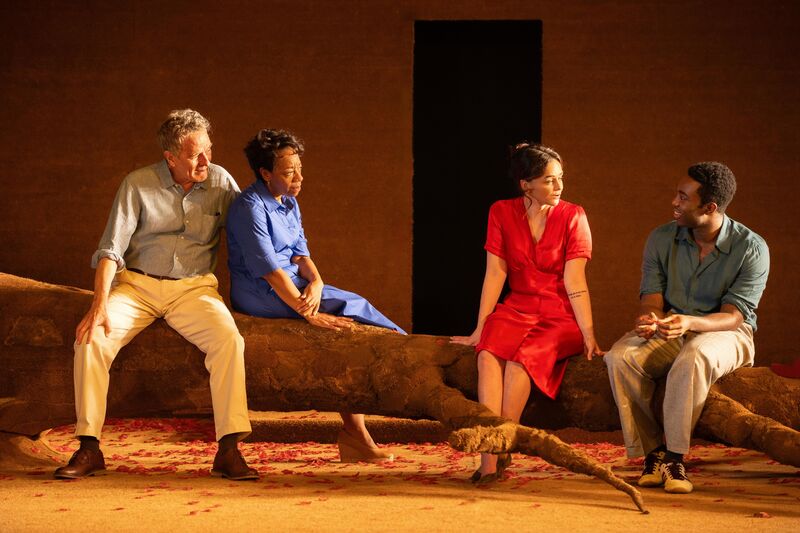 Four people sit on a tree trunk on stage