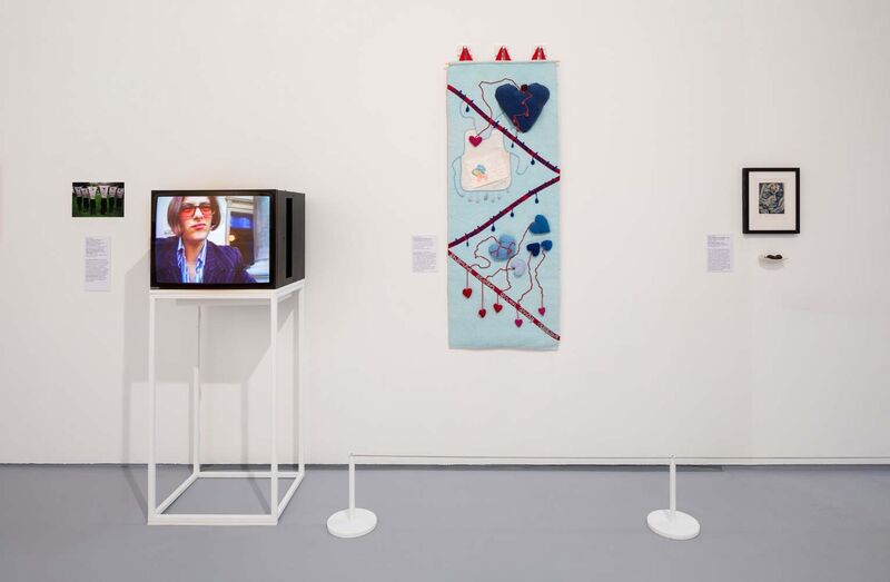 A gallery wall with a large embroidery and a TV sitting on a unit