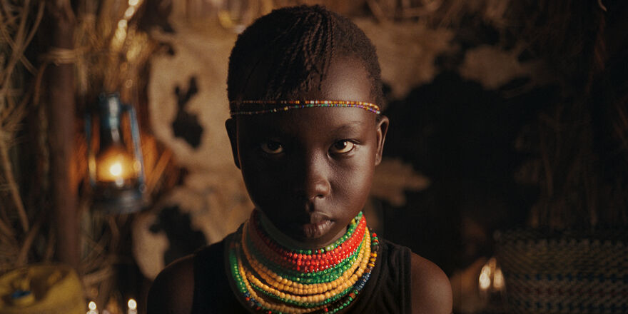 A girl in traditional Kenyan dress stares intently at the camera