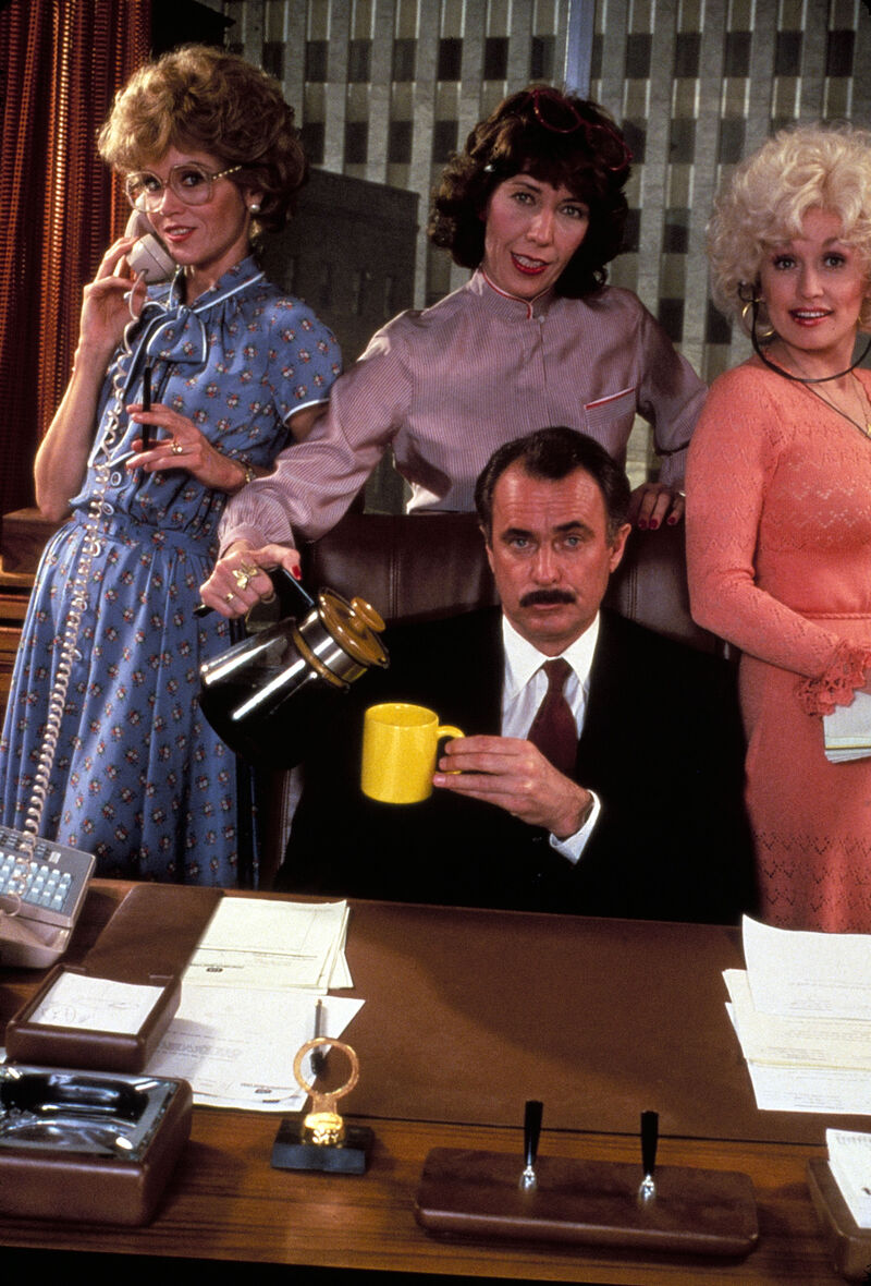 Three women stand behind a man sitting at a desk