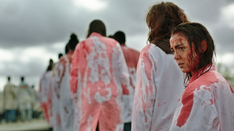 People standing in a queue outside wearing white lab coats cover in red