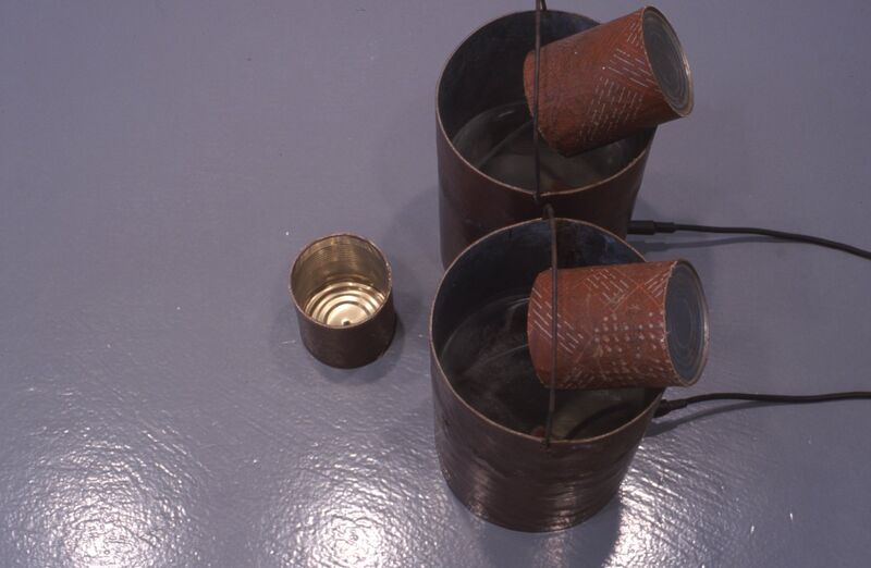 Metal buckets sit on a grey floor, with smaller cans within them.