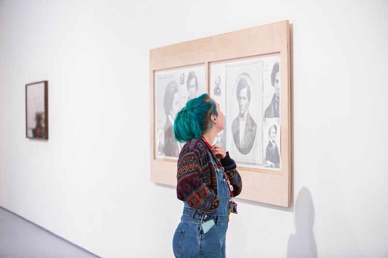 A person with blue hair looks up at a painting in DCA Galleries.