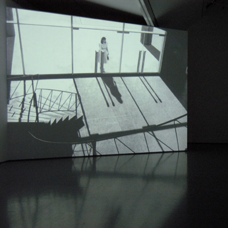 DCA Galleries during David Claerbout's exhibition. A projector screen shows a woman walking into an office building.