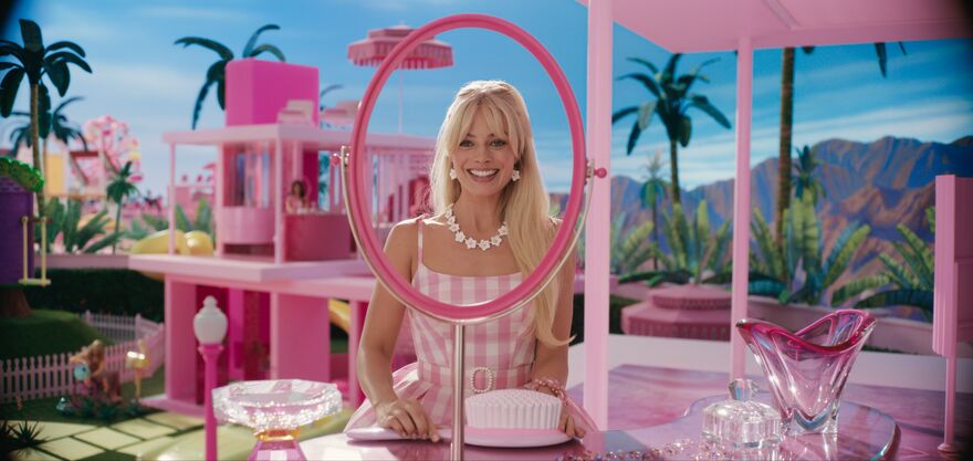Barbie looks in a pink mirror in Barbie land, which has blue skies and pink plastic furniture.