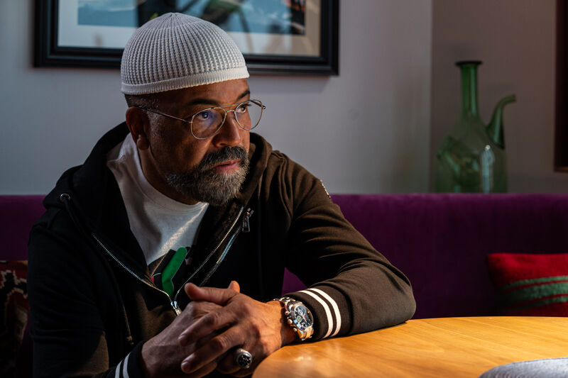 A man with a close-fitting cap, glasses and beard sits at a table.