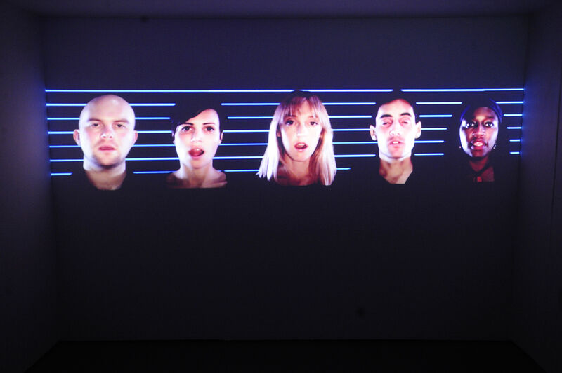 From Jaygo Bloom's exhibition. 5 people on a screen. Some have their mouths open as if they're singing. They are against a black background with blue lines through it.