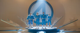 Three people and one man made out of rocks stand behind a giant number 4, all wearing blue suits with the number 4 on them.