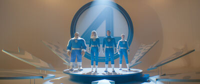 Three people and one man made out of rocks stand behind a giant number 4, all wearing blue suits with the number 4 on them.