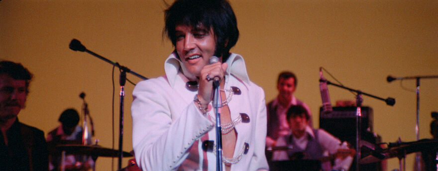 Elvis in white jumpsuit singing and smiling