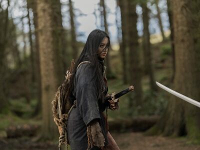A young woman stands in a forest holding a samurai sword.