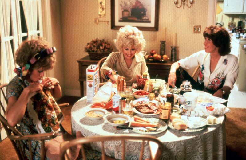 Three women sit around a table laughing while eating