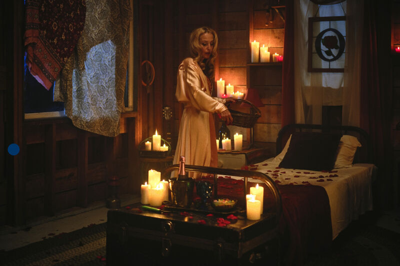 Woman sprinkling rose petals on a bed surrounded by candles