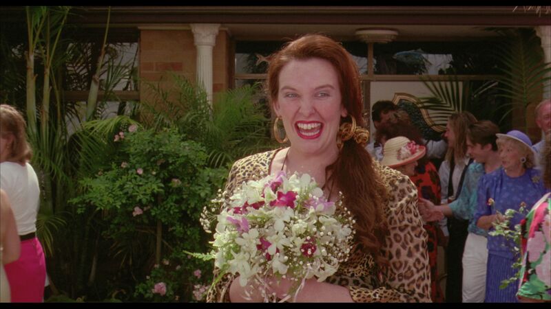 A young woman with gold hoop earrings, a leopard print shirt and bright lipstick clutches a bouquet.