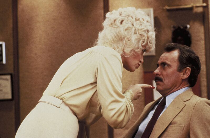 A blonde woman threatens a seated shamed-looking mustachioed older man