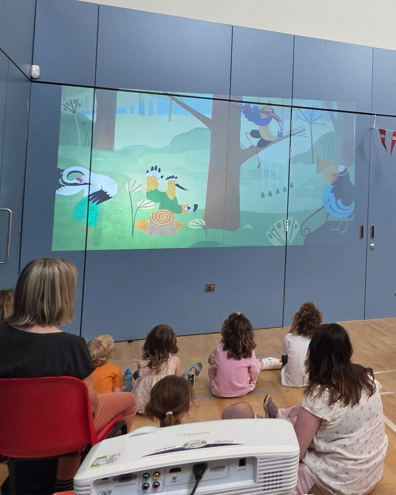 Children sit on the floor watching a projection of an animated film on the wall 