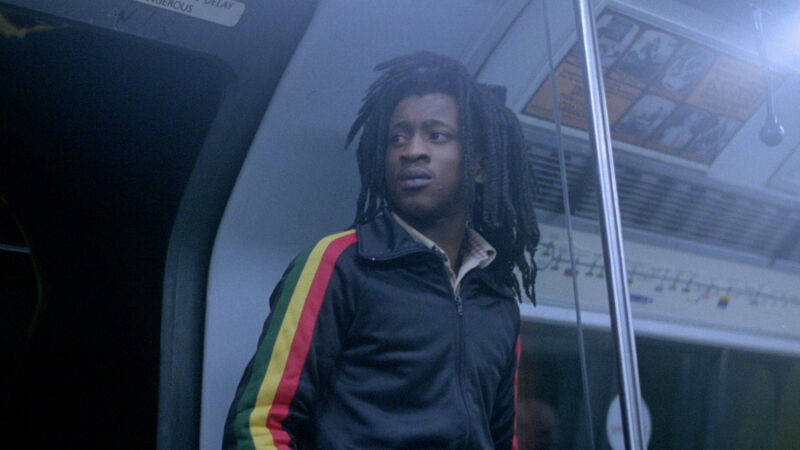 A young man with dreadlocks stands on an underground train