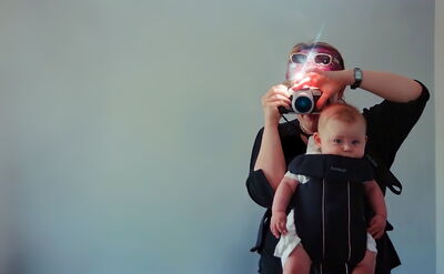 A mother photographs herself while carrying a baby in a sling