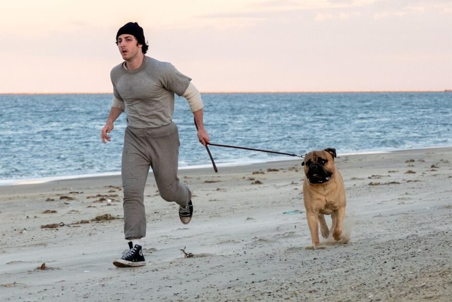 A young man runs along the beach with his dog