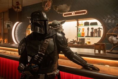 The Mandalorian, a man in space armour, with little alien Grogu on his shoulder.